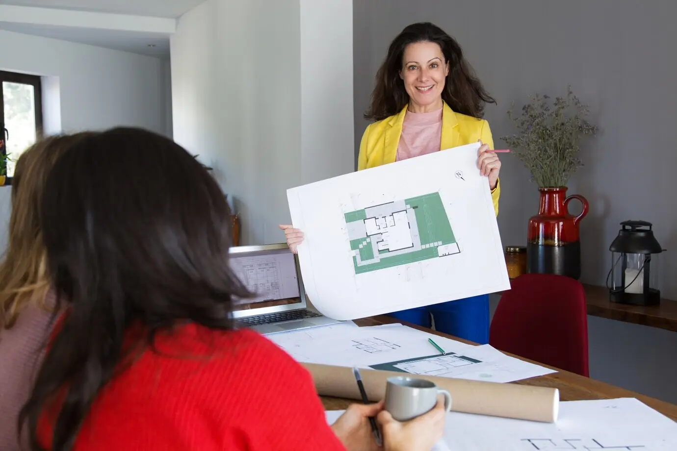 Ein lächelnder Architekt zeigt Kunden oder Kollegen einen Hausentwurf.